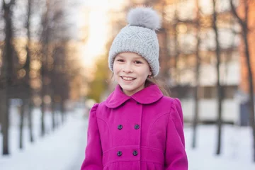 Foto op Aluminium Gelukkig jong meisje met plezier in een winterpark. Wintervakantie concept. Meisje buitenshuis. Gilr met een roze jas en gebreide muts die op een mooie dag loopt. © Albert Ziganshin