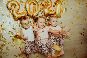 Children, 3 sisters, celebrate the new year 2021 at home, fool around and laugh in confetti. Celebrating New Years and Christmas at home during Covid-19 virus pandemic. Golden numbers and confetti