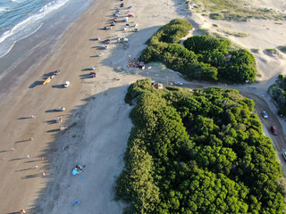 Vista aérea de la playa, con automóviles y personas descansando, durante el atardecer.