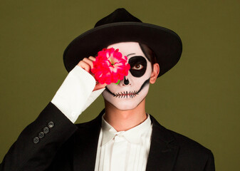 Young man wearing mexican day of the dead costume close eye with flower over green puffing cheeks with funny face. mouth inflated with air, crazy expression.