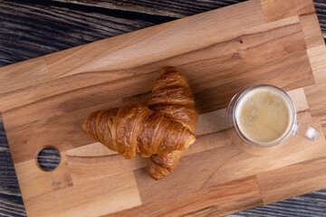 Croissants with a cup of coffee on a wooden board.