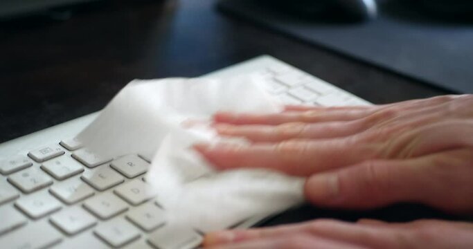Sanitizing bacteria and germs off dirty computer keyboard with an antibacterial disinfecting wipe to keep the family home clean and safe from contagious corona virus or germs.