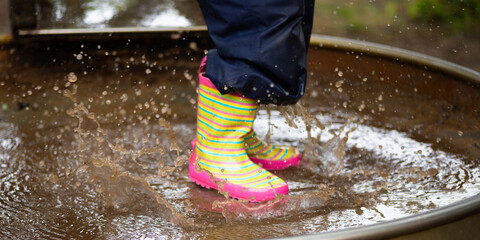 Detail of colorful rubber boots of a child jumping into a puddle of mud during a rainy and wet summer day