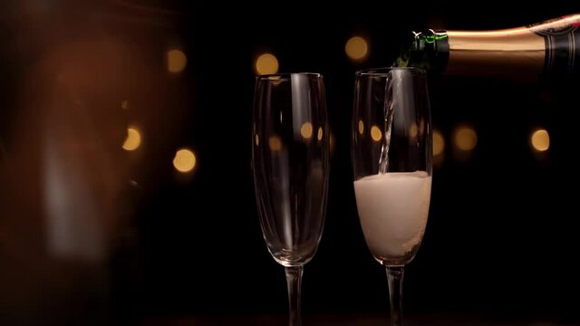 Close-up of the bartender pouring champagne into a glasses on a black background, the glass has a lot of foam and bubbles. Slow motion.Concept holiday, new year, Christmas, birthday.