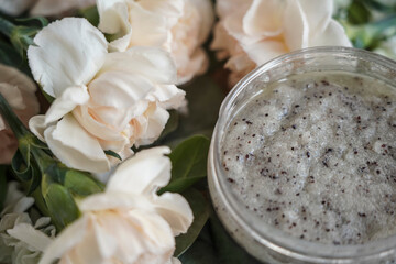 body scrub grey in a jar on a background of flowers