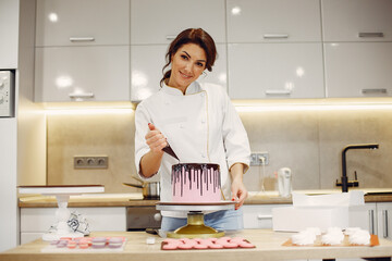 Confectioner in a kitchen. Woman in a uniform. Professional decorates the cake.