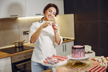 Confectioner in a kitchen. Woman in a uniform. Professional decorates the macaroni.