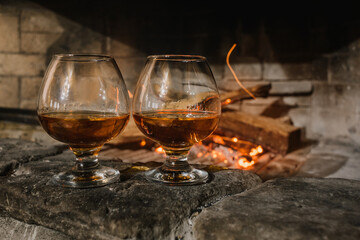 two glasses of cognac, brandy stands near the fireplace with an open fire, sparks of flame, a cozy evening in the chalet
