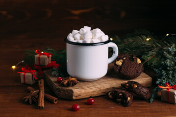 Enamelled cup of hot cocoa or coffee with marshmallows and cookies. Fir branches and christmas gifts.