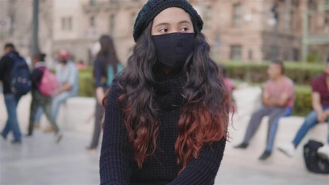 Vista de una adolescente sentada en las calles de la Ciudad de M&eacute;xico con ropa de abrigo y un cubrebocas en una tarde de oto&ntilde;o, covid19