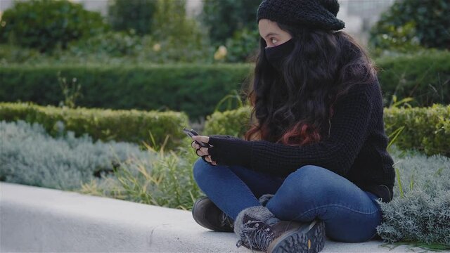 Vista de una adolescente en las calles de la Ciudad de M&eacute;xico con ropa de abrigo y un cubrebocas en una tarde de oto&ntilde;o, covid19, una ni&ntilde;a con su tel&eacute;fono celular jugando o enviando un mensaje