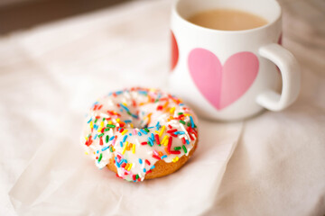Single Vanilla Donut with Colorful Sprinkles and a Mug with a Heart with Coffee and Cream