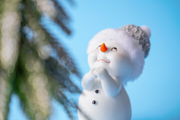 Close-up of a snowman on a blue background and on the background of a Christmas green tree. Toy...