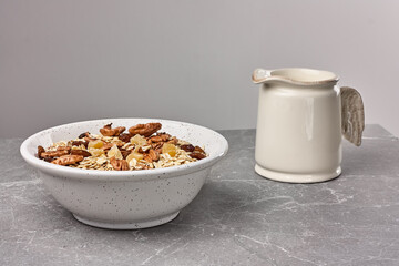 Healthy breakfast. Muesli or granola with dried fruits and pecans nuts in white bowl on gray stone table. Kinfolk style.