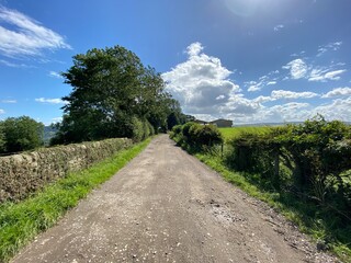 Dirt track road, with dry stone walls,  leading toward farm buildings, on a sunny day in, Newall with Clifton, Harrogate, UK