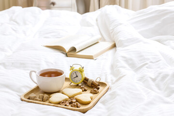 Fototapeta na wymiar Good Morning Wishes Concept. Breakfast in bed. Beautiful composition on a wooden tray: tea with cookies, nuts. Book on the blanket is the theme of a lazy, comfortable time at home. 9:00 am.