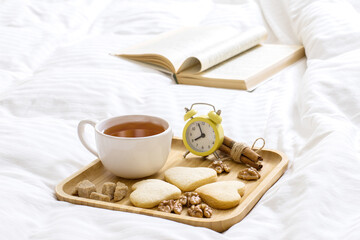 Good Morning Wishes Concept. Breakfast in bed. Beautiful composition on a wooden tray: tea with cookies, nuts. Book on the blanket is the theme of a lazy, comfortable time at home. 9:00 am.