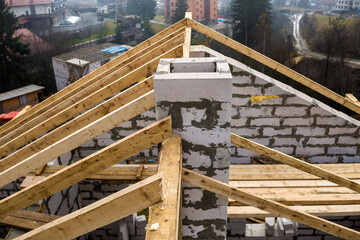 Close-up detail of roof frame of rough wooden lumber beams and chimney made of foam insulation blocks on blurred green background. Building, roofing, construction and renovation concept.