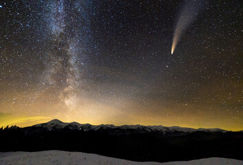 Surreal view of night in mountains with starry dark blue cloudy sky and C/2020 F3 (NEOWISE) comet...