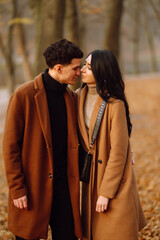 Young couple in love holding hands and walking through a forest on a  autumn day. Beautiful stylish couple enjoying autumn weather in the park. The concept of youth, love, freedom.