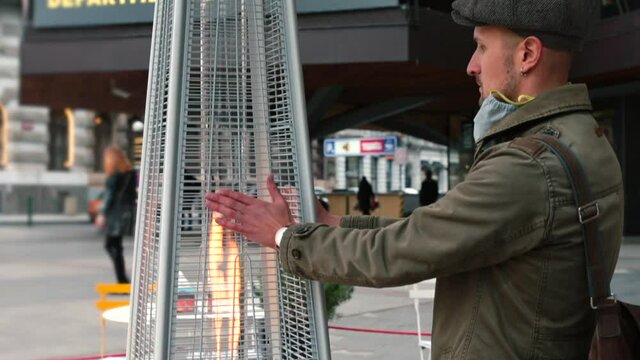 Young man warms his hands with outside heater fire. Compared to standard heating systems, going green is better for the environment because it helps eliminate greenhouse gasses. Eco-friendly heating.