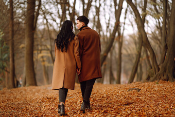 Young couple in love holding hands and walking through a forest on a  autumn day. Beautiful stylish couple enjoying autumn weather in the park. The concept of youth, love, freedom.