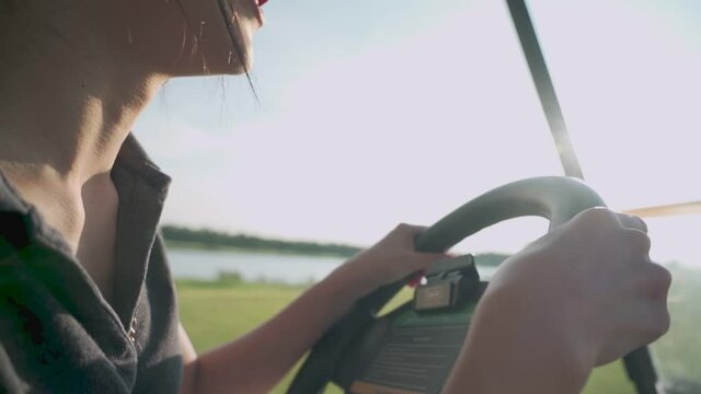 close up shot of young asian female golfer smile and happy while driving golf car inside beautiful green golf course, having fun relax on holidays summer vacation, spring valley, hot sunny weather