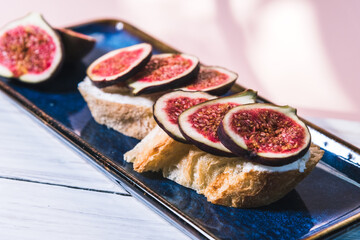 Bruschetta of baguette, cheese and figs are on a plate on the table. The concept of minimalism in food