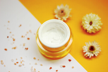 Natural skincare cream on a yellow background with flowers