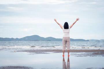 Obraz premium Asian woman raise hand up alone on the beach. concept for holiday vacation and refreshing.