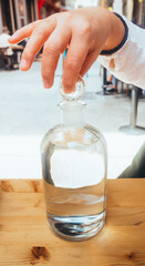 Close-up view of a woman's hand opening a glass bottle filled with water on a wooden table