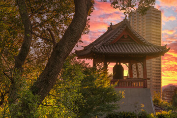 Sunset on the Shōrō bell at the foot of Daibutsu Mount in Ueno Park known as Time Bell of Kaneiji Temple made famous by Matsuo Basho with skyscraper in background.