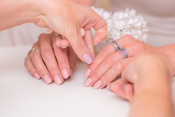 Manicurist holding female hands with wedding manicure nails, nude gel polish and white flowers