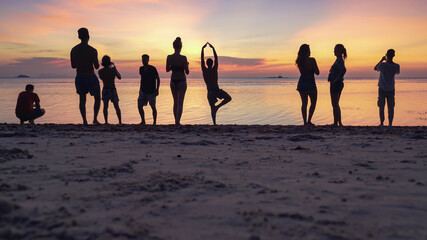 Silhouettes of people on the sandy beach enjoying the sunset and taking pictures on smartphones against the background of the sea