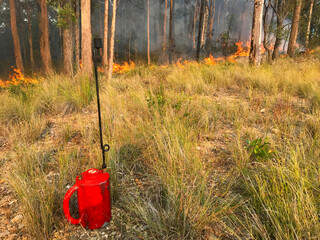 A drip torch with fire in the background