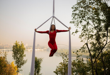 silhouette of a beautiful and professional Aerial silk artist practicing in the red suit under the famous glass bridge over the Kiev city attracting people to see her show