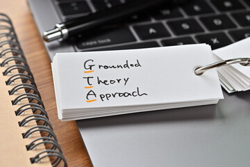 The words "GTA" written in a word book with laptop PC and a pen. It is an acronym for "Grounded Theory Approach".