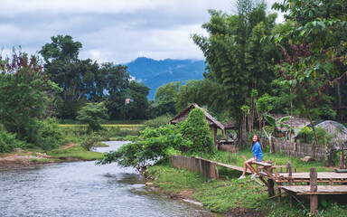 Portrait image of a beautiful asian woman sitting by the river with mountains and nature background