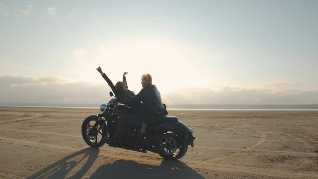 Guy with a girl on a motorcycle in the desert. Couple riding on vintage motorcycle and having a good time at sunset on a dry salt lake. Slow motion shot