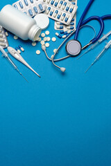 Stethoscope, syringe, thermometer and can of pills on blue background top view with copy space