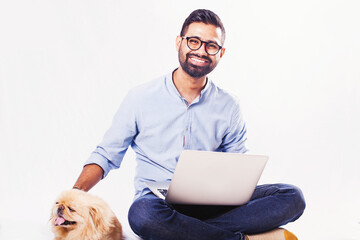 Young Indian man with pekingese dog using computer for the vet consultation over white background
