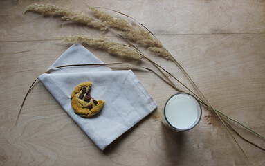 Chocolate chip cookies on a wooden background with a glass of milk and a linen napkin.