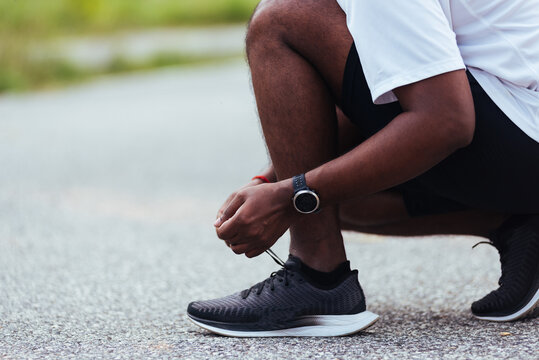 Stockfoto med beskrivningen Close up Asian sport runner black man wear  watch sitting he trying shoelace running shoes getting ready for jogging  and run at the outdoor street health park, healthy exercise