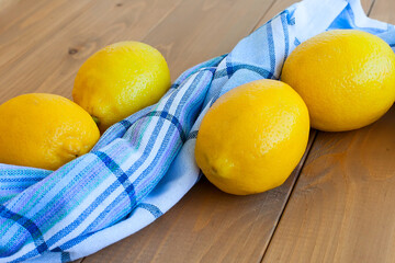 Still life of big ripe yellow lemons lying on checkered towel with glass of lemon juice on windowsill in sunlit room.