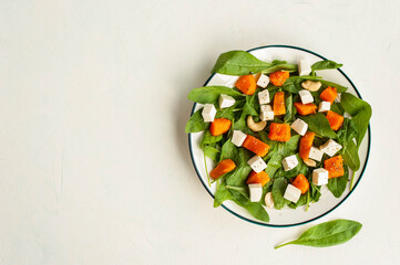 Bright autumn salad with pumpkin, spinach and feta cheese on a light concrete background. Diet healthy food. View from above. A place for text.