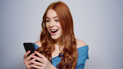 Fototapeta premium Excited woman receiving good news indoors. Happy girl texting message in studio