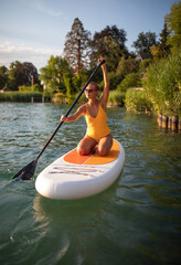 SUP Stand up paddle board concept - Pretty, young woman paddle boarding on a lovely lake in warm...