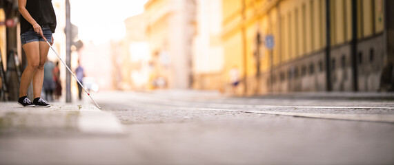 Blind woman walking on city streets, using her white cane to navigate the urban space better and to...