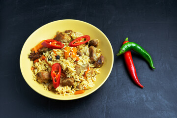 Asian pilaf on a yellow plate with green and red peppers. Dark background.
