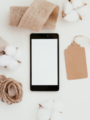 Smartphone mockup on white background with brown cardboard label, linen and cotton around